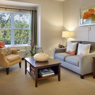 A cozy and well-lit living room featuring a sofa, armchair, coffee table, and a large window with curtains.
