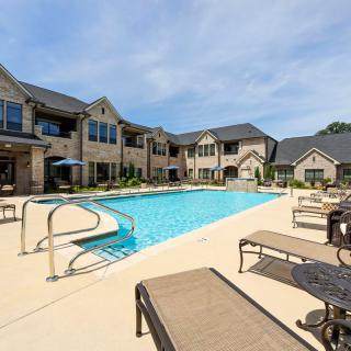 An outdoor swimming pool with loungers at an apartment complex on a sunny day.