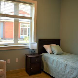 A simple bedroom with a single bed, nightstand, and a window letting in natural light.