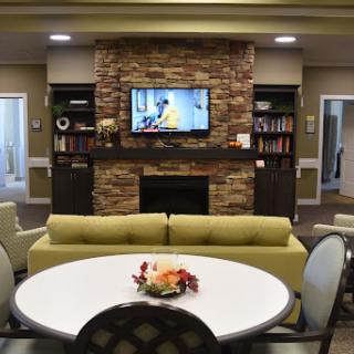 A cozy living room space featuring a green sofa, a dining table, and a television mounted above a stone fireplace.