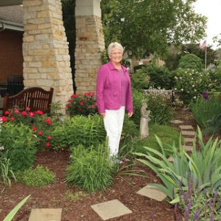 A woman standing gracefully in a vibrant garden filled with flowers and greenery.