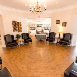 A modern waiting room featuring comfortable leather chairs, wooden flooring, and a chandelier.