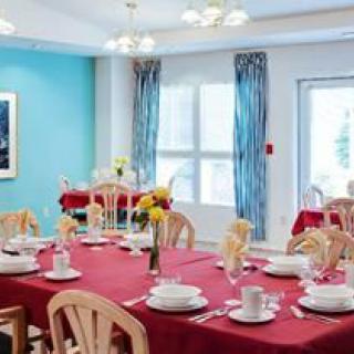 A neatly arranged dining room with tables set for a meal, featuring red tablecloths and wooden chairs.