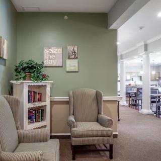 A cozy interior space with two armchairs, a small bookshelf, and wall art against a green-painted wall.