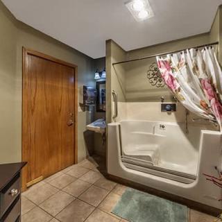 A bathroom with a walk-in tub, tiled floor, and wooden door.