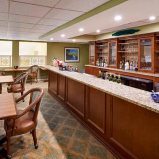 A cozy bar interior featuring a long counter with chairs, displaying bottles and glasses.