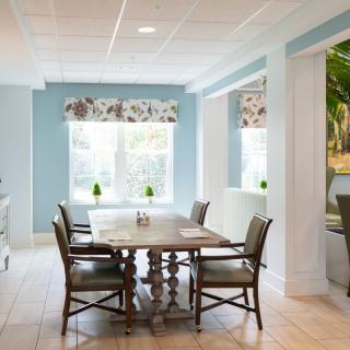 A bright dining area with a wooden table, surrounded by chairs and adorned with floral window treatments.