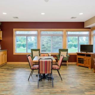 A cozy dining and living room space with large windows, comfortable seating, and a television.