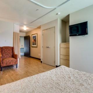 A well-lit hotel room with a comfortable chair, wall-mounted TV, and a neatly made bed.