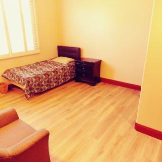 A minimalist bedroom with a single bed, nightstand, and wooden flooring.
