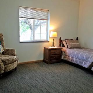 A simple bedroom with a single bed, armchair, and a window letting in natural light.