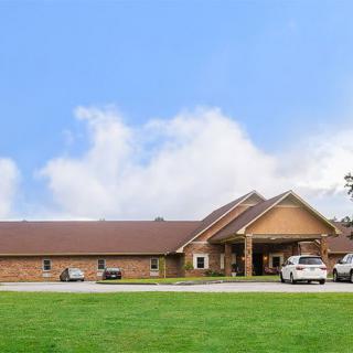 A large brick building with a parking lot, surrounded by green grass and under a clear blue sky.