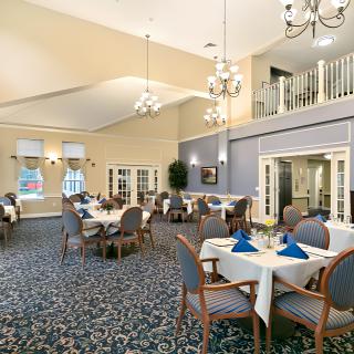 A spacious and elegantly decorated dining room with neatly arranged tables and chairs, featuring chandeliers and a patterned carpet.