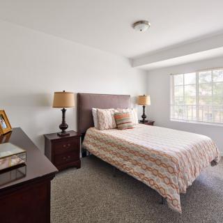 A bright bedroom with a neatly made bed, flanked by nightstands and lamps, featuring a window that lets in natural light.