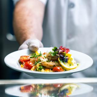 A chef presents a beautifully plated gourmet dish with vibrant colors and fresh ingredients.
