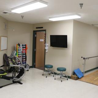 A well-equipped physical therapy room featuring exercise equipment, chairs, and a TV for patient use.