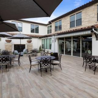 A spacious outdoor patio area with tables, chairs, and large umbrellas, set against the backdrop of a building with a stone facade.