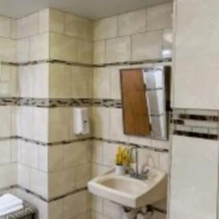 A tiled bathroom with a small sink, mirror, and soap dispenser.