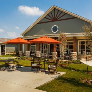 A charming building with an outdoor seating area featuring orange umbrellas, surrounded by a well-maintained lawn under a clear blue sky.