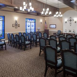 A chapel interior with rows of chairs, stained glass windows, and chandeliers.