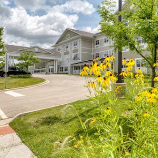 A serene view of a residential building surrounded by vibrant flowers and lush greenery under a cloudy sky.