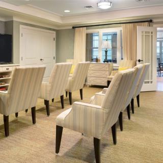 A well-lit conference room with several rows of upholstered chairs facing the front.
