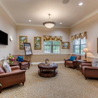 A cozy living room with several armchairs and a coffee table, decorated with artwork and large windows.