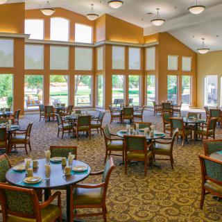 A spacious dining room with large windows, elegant tables and chairs, and bright lighting.