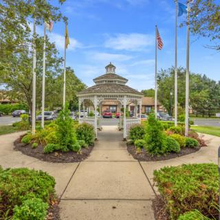 A well-landscaped area with a gazebo, surrounded by flags and greenery under a clear blue sky.