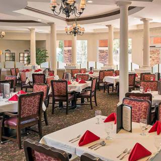 An elegant dining area featuring well-set tables with red napkins and a chandelier overhead.