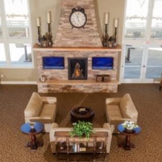 A cozy living room with a central seating area, featuring armchairs and tables around a fireplace with a clock above it.