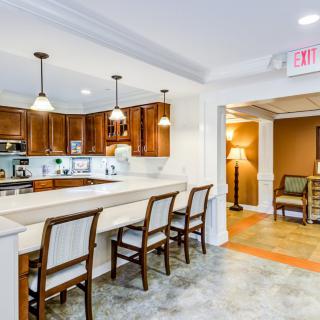 A modern kitchen with wooden cabinets and a long dining countertop equipped with several chairs. Pendant lights illuminate the space, offering a cozy atmosphere.