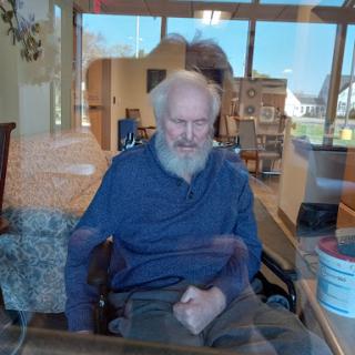 An elderly man sitting in a wheelchair, lost in thought as sunlight filters through the window.