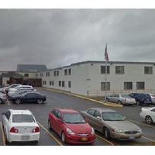 A parking lot with several cars parked in front of a large building under an overcast sky.