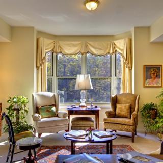 A cozy living room with two armchairs, a lamp on a small table, and large windows with curtains.