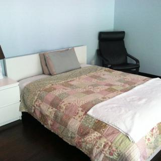 A cozy bedroom with a bed, chair, and bedside table featuring a lamp.