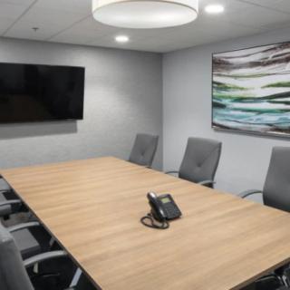 A modern conference room with a large meeting table, chairs, and a TV screen.