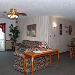 A cozy living room with a patterned sofa, wooden table, and ceiling fan.