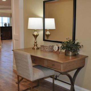 A cozy home office setup featuring a wooden desk with a lamp, mirror, and chair.