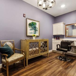 A stylish salon room with modern decor, featuring a comfortable chair, artwork on the wall, and elegant wood flooring.