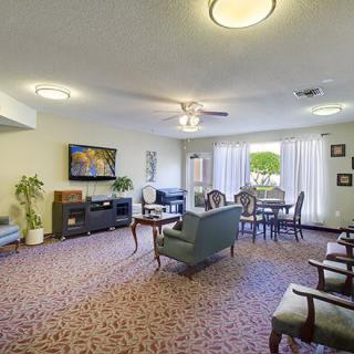 A cozy living room with a television, comfortable seating, and natural light from large windows.