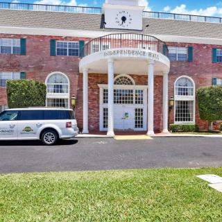 A brick building with a grand entrance featuring columns and a white car parked outside.