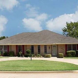 A suburban single-story brick house with a well-maintained lawn and driveway.