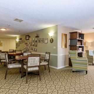 A cozy interior space featuring a dining area with tables and chairs, adjacent to a lounge area with a bookshelf and comfortable seating.