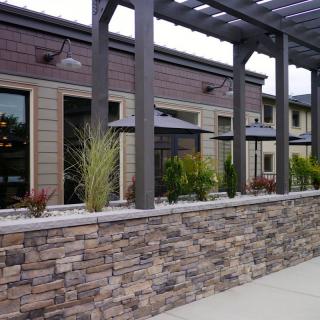 A modern building with a stone wall and landscaped exterior, featuring a pergola and decorative plants.
