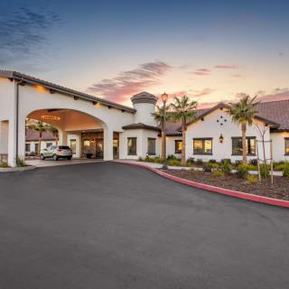 A modern building with an arched entrance and driveway, set against a sunset sky.