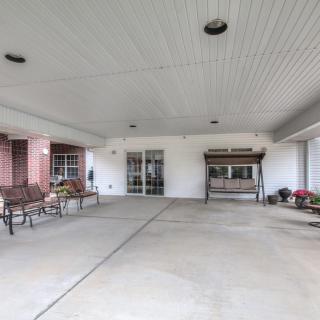 A covered entrance area with benches and a swing, featuring a concrete floor outside a building.