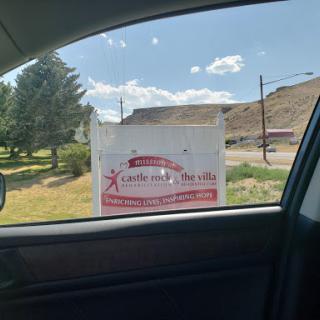 A business sign viewed from inside a car, set against a clear sky and grassy area.