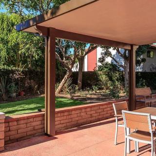 A sunny backyard patio with outdoor seating, surrounded by a garden and trees.
