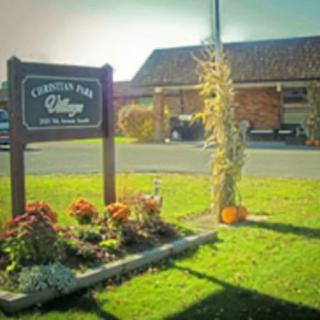 A village sign surrounded by flowers and autumn decorations near a building.